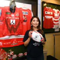 Pop singer Atsuko Watase poses with a ball in front of autographed replica rugby jerseys at a rugby bar in Yokohama during an interview with The Japan Times on July 3. | YOSHIAKI MIURA