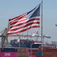 The U.S. flag flies over a container ship unloading its cargo from Asia at the Port of Long Beach, California, on Thursday. | AFP-JIJI