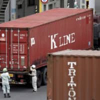 Workers stand near a truck hauling a Kawasaki Kisen Kaisha Ltd. \"K\" Line shipping container at a shipping terminal in Yokohama on July 11. | BLOOMBERG
