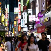 People walk past illuminated stores at the Myeongdong shopping district at night in Seoul on June 28. | BLOOMBERG