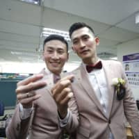 A couple holding identity cards pose for photographs while registering for marriage at a Household Registration Office in Taipei on May 24. | BLOOMBERG