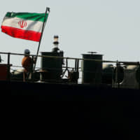 A crew member raises the Iranian flag on the oil tanker Adrian Darya 1, previously named Grace 1, as it sits anchored in the Strait of Gibraltar on Sunday. | REUTERS