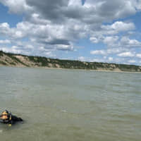 A Royal Canadian Mounted Police (RCMP) diver, part of the law enforcement team looking for fugitive murder suspects Kam McLeod and Bryer Schmegelsky, searches the Nelson River after a damaged aluminum boat was found nearby in Sundance, Manitoba, Sunday. | MANITOBA RCMP / HANDOUT / VIA REUTERS