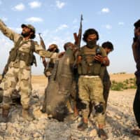 Rebel fighters pose for a picture with the remains of a downed regime warplane near the jihadi-held Syrian town of Khan Sheikhun in the south of Idlib province on Wednesday. | AFP-JIJI