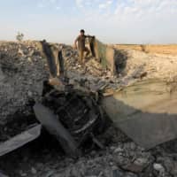 A rebel fighter stands near the remains of a downed regime warplane near the jihadi-held Syrian town of Khan Sheikhun in the south of Idlib province on Wednesday. | AFP-JIJI