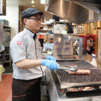 Xia Gang, a Chinese manager of a Bronco Billy restaurant in Nagoya\'s Moriyama Ward, grills a Hamburg steak at the restaurant. | CHUNICHI SHIMBUN