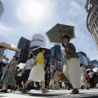 Parasols help pedestrians beat the heat in the Ginza district of Tokyo on Aug. 7. | KYODO