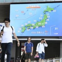 People walk below a large screen in Tokyo\'s Akiharaba district on Saturday that shows temperatures were forecast to rise above 30 C across the nation that day. | KYODO