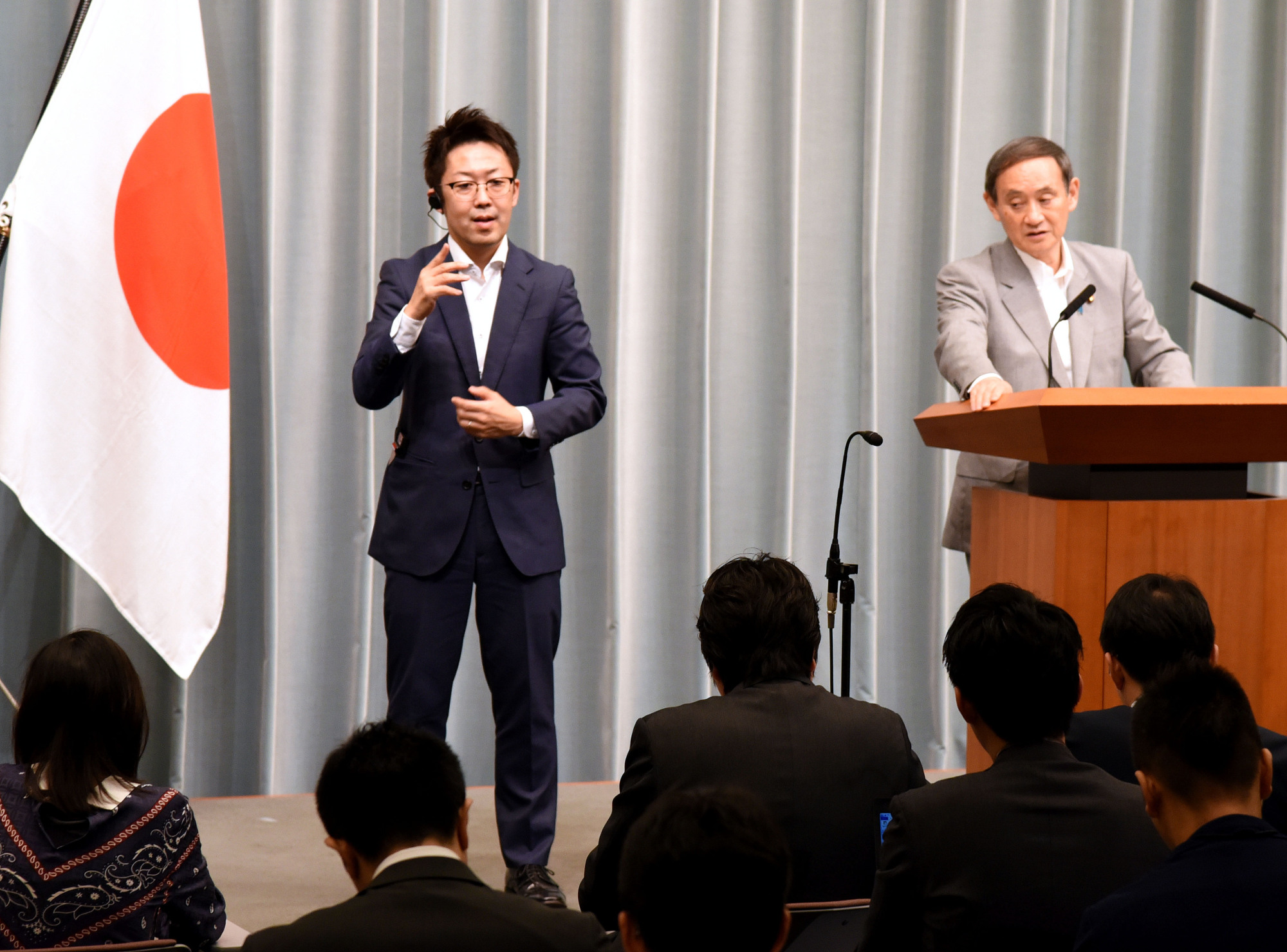 Kohei Ehara, a sign language interpreter, works beside Chief Cabinet Secretary Yoshihide Suga during a news conference at the Prime Minister's Office in Tokyo on June 20. | SATOKO KAWASAKI