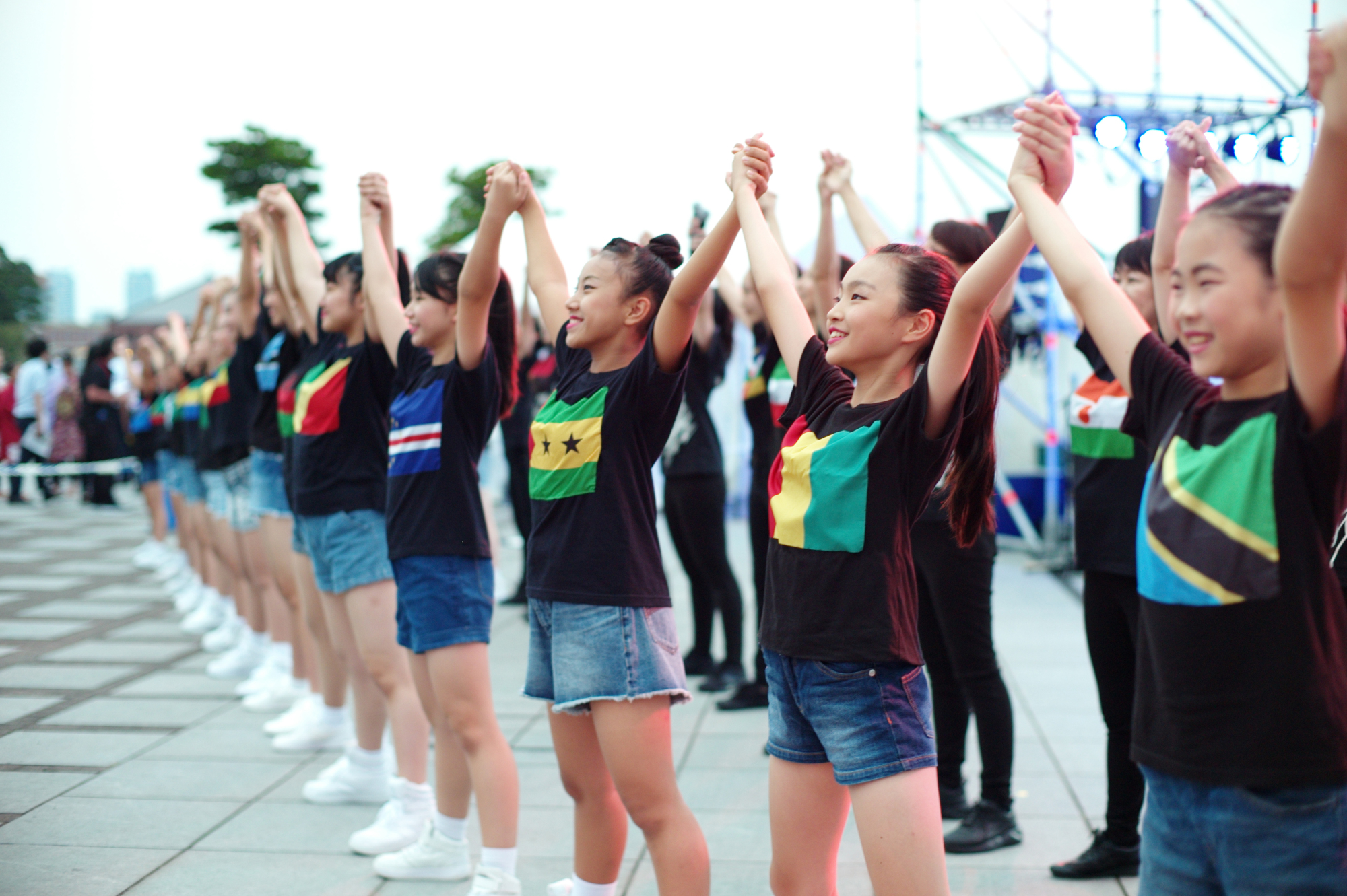 Girls wearing T-shirts with African national flags hold and raise their hands Tuesday during a summer dance festival in Yokohama to mark the kickoff of the seventh Tokyo International Conference on African Development, which opens Wednesday. Dozens of top African leaders will come to the port city hosting the three-day summit meeting. | RYUSEI TAKAHASHI