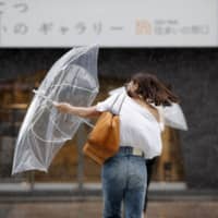 A woman is caught in strong wind and rain on Tuesday morning in the city of Fukuoka after Typhoon Francisco made landfall on Kyushu. | KYODO