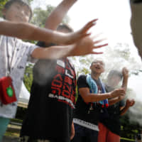 Children in Tokyo on July 25 enjoy a large-scale misting tower dispensing ultra-fine mist during a proving test of heat countermeasures for the 2020 Olympic and Paralympic Games. | REUTERS