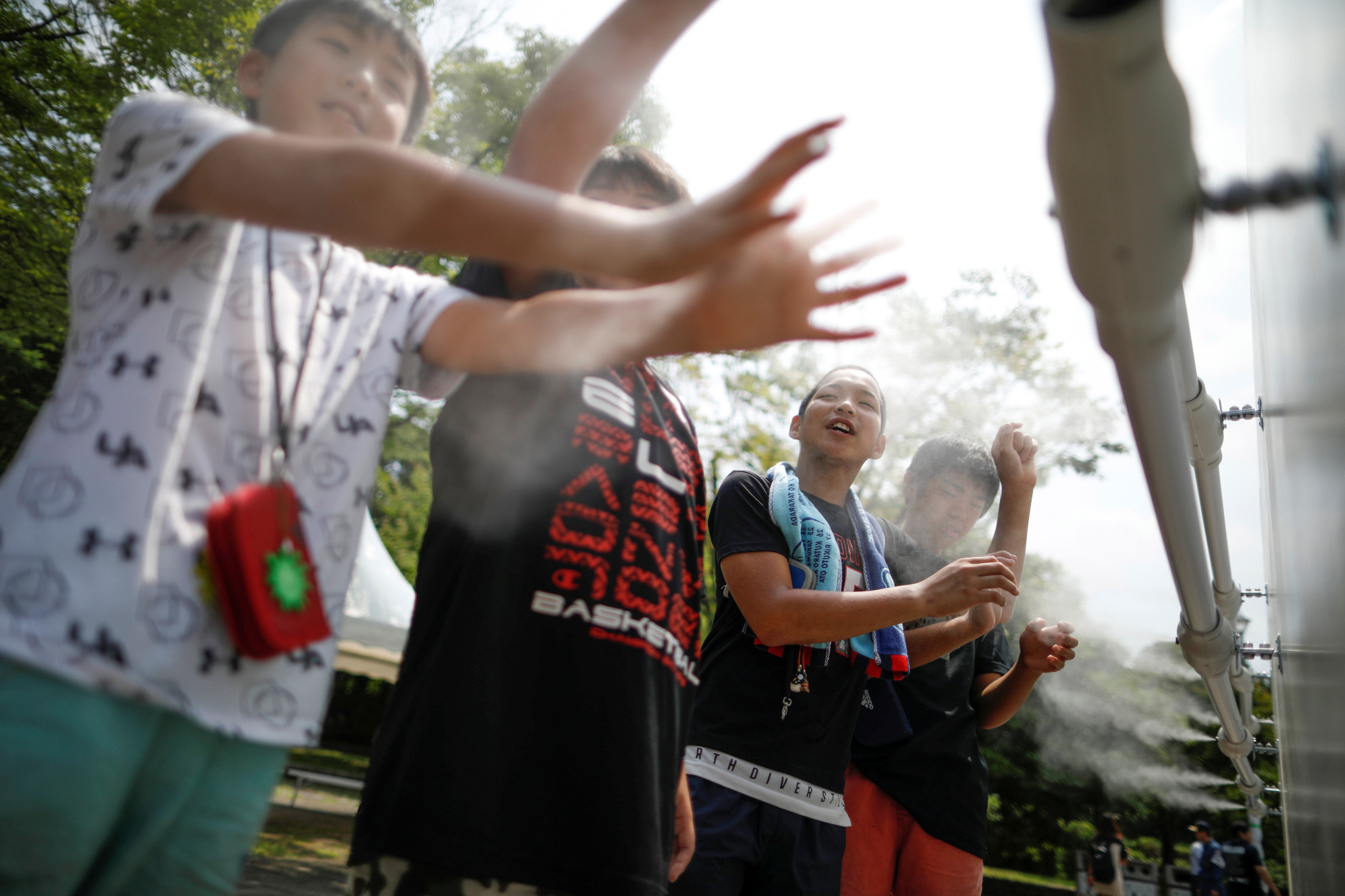 Children in Tokyo on July 25 enjoy a large-scale misting tower dispensing ultra-fine mist during a proving test of heat countermeasures for the 2020 Olympic and Paralympic Games. | REUTERS