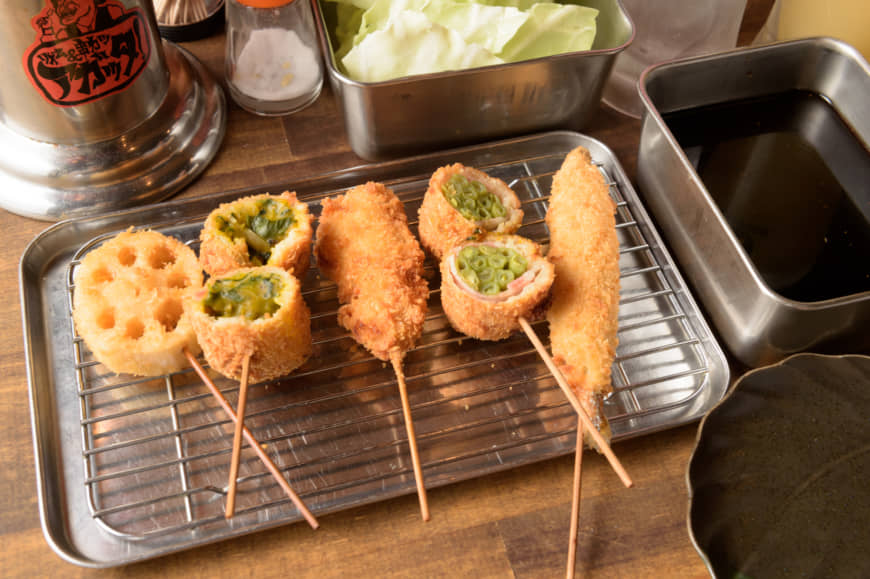This food's got soul: A lineup of Rhythm and Kushikatsu Agatta's skewers, including (from left) renkon (lotus), kabocha benjukushi (mashed pumpkin filled with vegetables), tori (chicken), ingen bēkon-maki (string beans wrapped in bacon) and shishamo (smelt). | TSUYOSHI TAGAWA