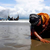 An exhausted Rohingya refugee woman touches the shore in Bangladesh after crossing the border from Myanmar through the Bay of Bengal in September 2017. | REUTERS