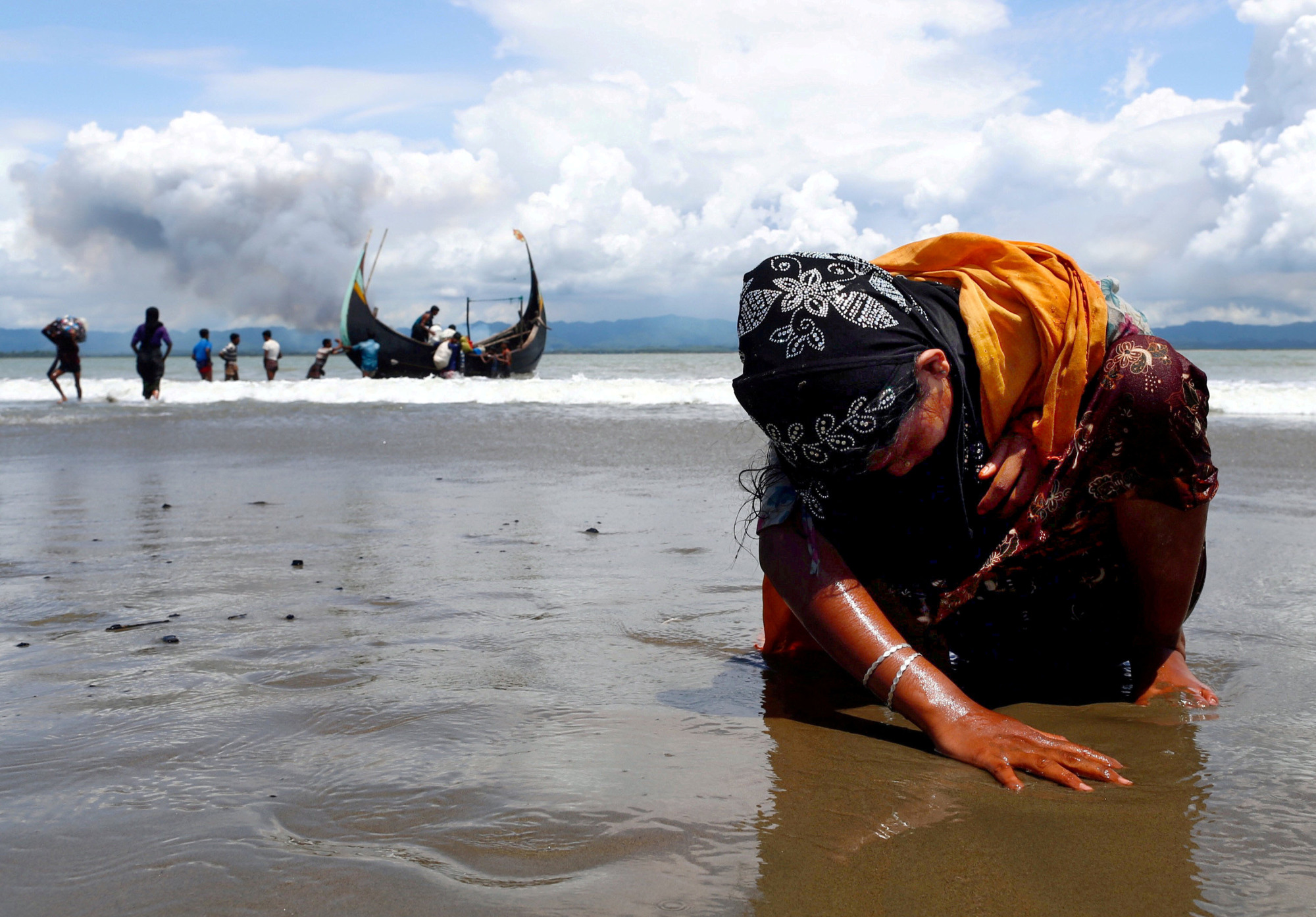 An exhausted Rohingya refugee woman touches the shore in Bangladesh after crossing the border from Myanmar through the Bay of Bengal in September 2017. | REUTERS