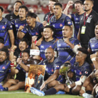 The Brave Blossoms celebrate after their victory over Tonga on Saturday night in Higashiosaka, Osaka Prefecture. Captain Michael Leitch is holding a photo of head coach Jamie Joseph and his mother, who passed away earlier in the day in New Zealand, as the team poses for photos. | KYODO