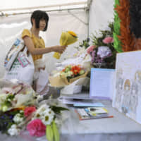 One month after an arson attack on Kyoto Animation Co.\'s studio in Kyoto killed 35 people, a woman places flowers Sunday at an altar set up to honor the victims near the site of the incident. The outpouring of support for the company continues to grow. | KYODO