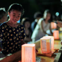 A girl looks at a lantern to be floated on the Sumida River at the annual Toro Nagashi Festival in Tokyo\'s Sumida Ward on Saturday evening. The festival began in 1946 to honor the war dead, especially the masses of people who drowned in the river while fleeing the devastating firebombings of Tokyo. In recent times, people inscribe wishes on the lanterns. | RYUSEI TAKAHASHI