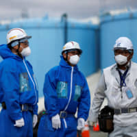 Workers stand in front of storage tanks for radioactive water at the tsunami-crippled Fukushima No. 1 nuclear power plant in Okuma, Fukushima Prefecture, in February. | REUTERS