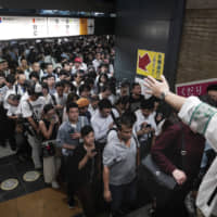 Station attendants guide commuters shortly after train platforms re-opened following delays on Monday morning due to a powerful typhoon that passed over Tokyo, halting major train lines. | AP