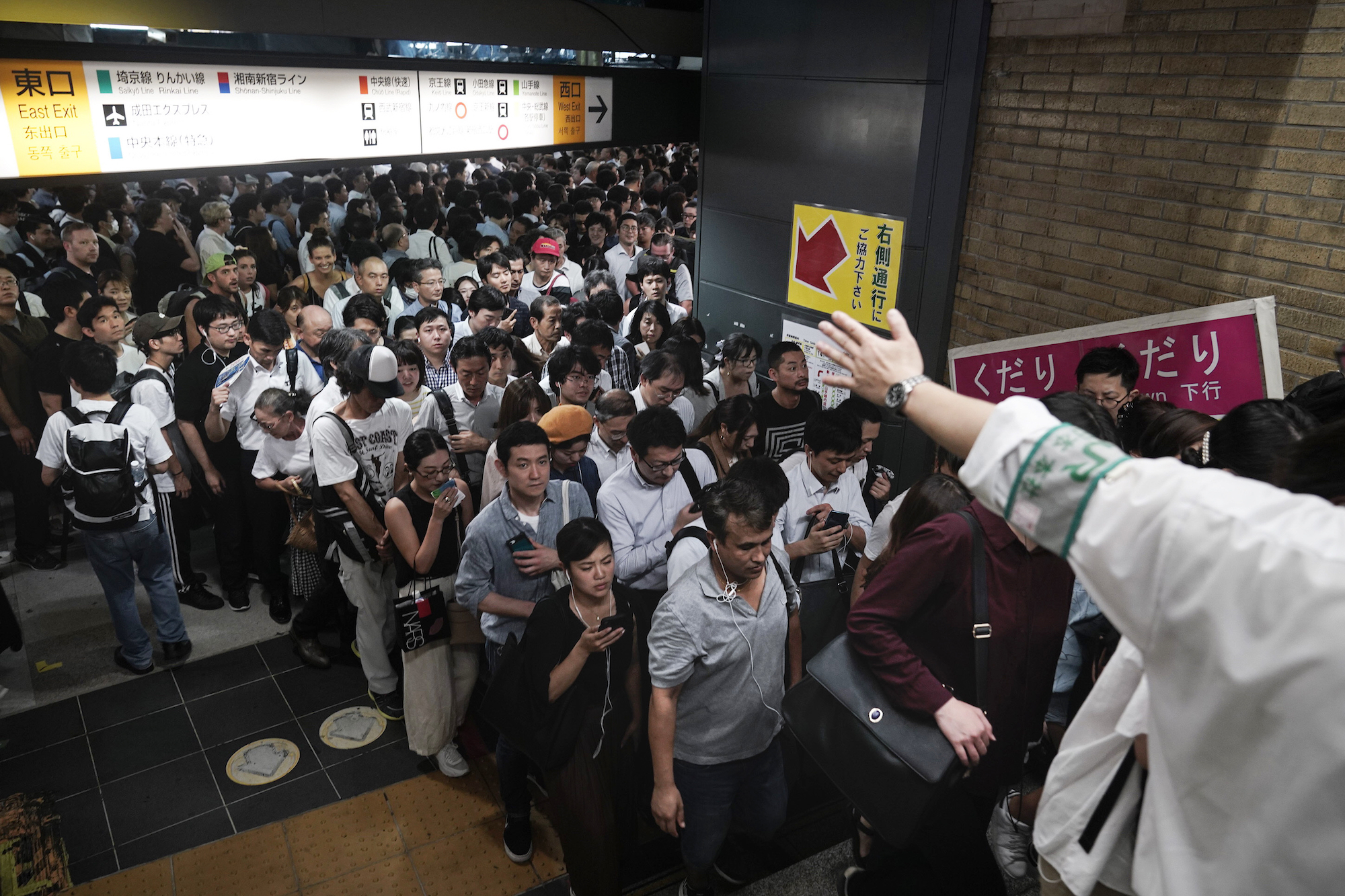 Station attendants guide commuters shortly after train platforms re-opened following delays on Monday morning due to a powerful typhoon that passed over Tokyo, halting major train lines. | AP