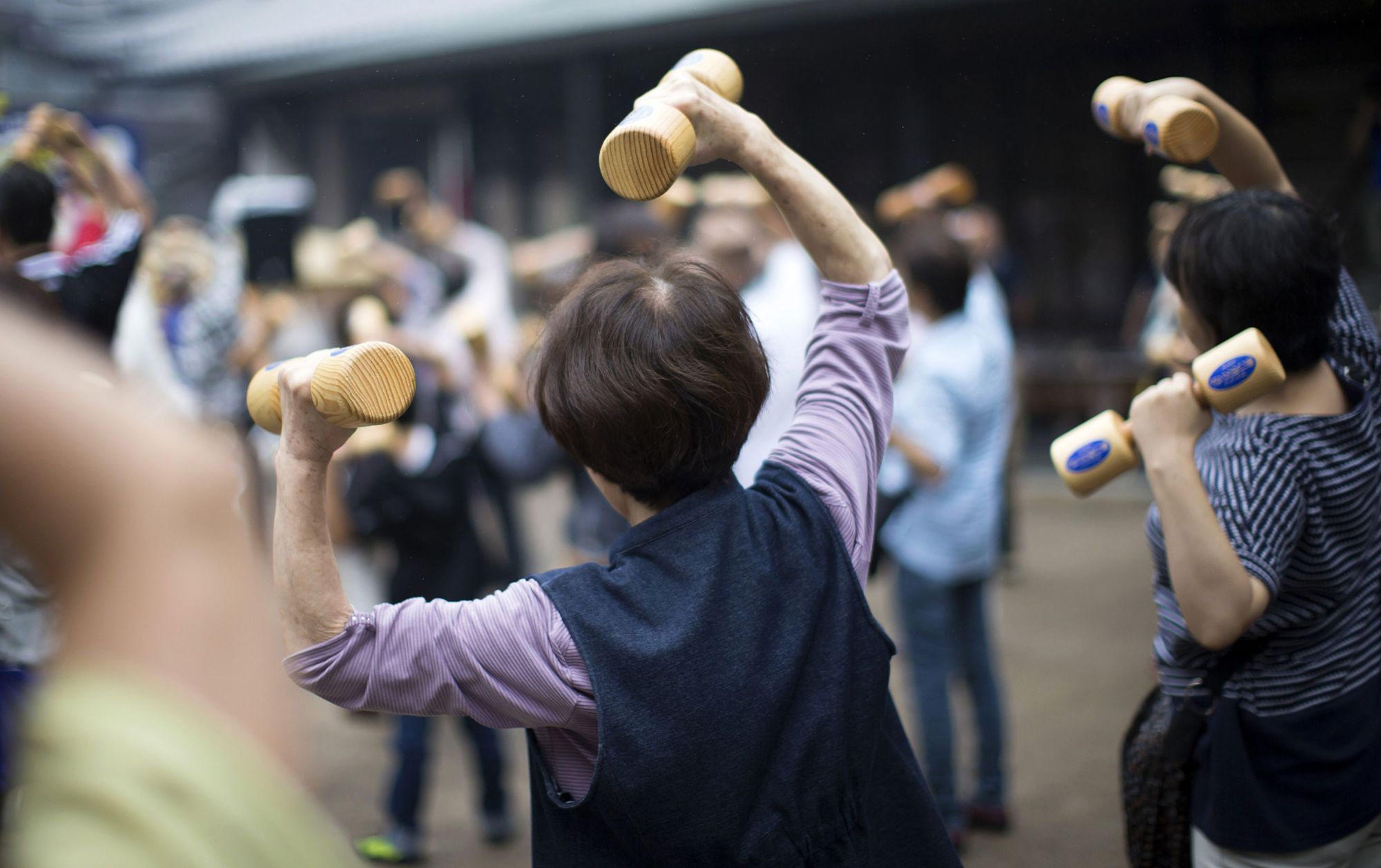 People holding wooden dumbbells exercise during an event at a temple in the Sugamo district of Tokyo. | BLOOMBERG