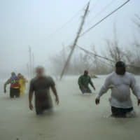 Volunteers walk under the wind and rain from Hurricane Dorian through a flooded road as they work to rescue families near the Causarina bridge in Freeport, Grand Bahama, Bahamas, Tuesday. The storm\'s punishing winds and muddy brown floodwaters devastated thousands of homes, crippled hospitals and trapped people in attics. | AP