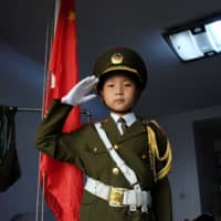Feng Jianhan, 9, poses for a picture in military uniform next to a Chinese flag that he raises every morning via a rope and pulley at his home in Xian, China, on Thursday. | REUTERS