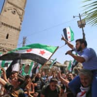 Men wave flags of the Syrian opposition and chant slogans during a demonstration against the Syrian regime in the town of Maaret al-Numan in the northwestern Idlib province on Sept. 6. | AFP-JIJI