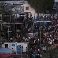 Refugees and migrants are seen around burned containers following a fire in the Moria camp on the island of Lesbos, Greece, Sunday. | REUTERS