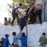 Refugees and migrants try to escape the camp of Moria after a fire broke out in the camp in Mytilene on the Greek island of Lesbos Sunday. | AFP-JIJI