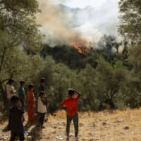 Refugees and migrants look at a fire that broke out in the camp of Moria Sunday on the Greek island of Lesbos. | AFP-JIJI