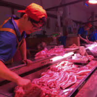 A clerk stacks cuts of pork at a meat market in Beijing on Sept. 11. | AP