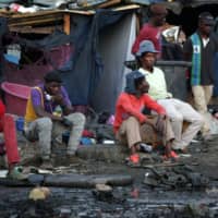 Foreign nationals sit and watch after their shacks were set alight by alleged looters at Marabastad, near the Pretoria Central Business District (CBD) in Pretoria, South Africa, on Monday. | AFP-JIJI