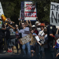 Demonstrators stand along the motorcade route of President Donald Trump as he leaves a fundraiser, Tuesday in Portola Valley, California. | AP