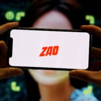 The logo of the Chinese app Zao, which allows users to swap their faces with celebrities and anyone else, is seen on a mobile phone screen in front of an ad for the app. | REUTERS