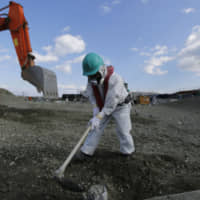 A worker wearing a protective suit and a mask levels ground at the tsunami-crippled Fukushima No. 1 nuclear power plant in the town of Okuma, Fukushima Prefecture, in February 2016. | VIA BLOOMBERG