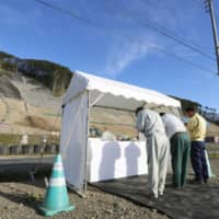 People on Friday mourn victims of an earthquake that hit the town of Atsuma, Hokkaido, and surrounding areas on Sept. 6 last year. The area where the quake triggered landslides is seen in the background. | KYODO