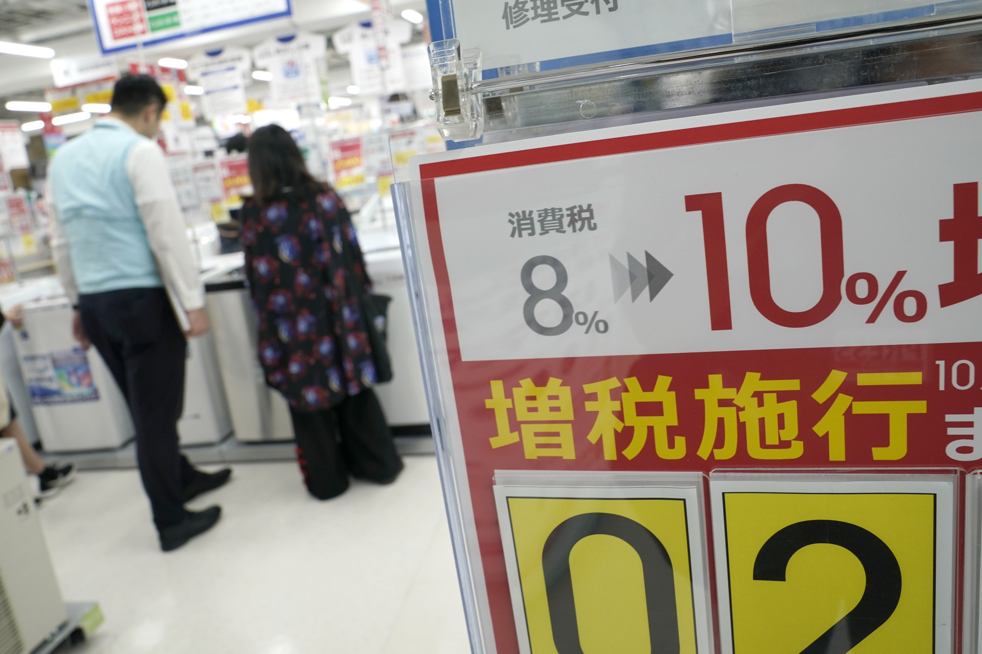 A display on the consumption tax increase is seen as a customer and employee look at washing machines displayed for sale at an electronics store in Tokyo on Sept. 5. | BLOOMBERG