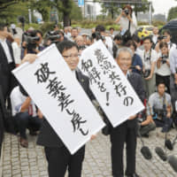 Lawyers representing fishermen hold up signs in front of the Supreme Court in Tokyo on Friday. One says that the case — a long-running saga over the fate of a dike in Isahaya Bay, Nagasaki Prefecture — has been sent back to a lower court, while the other calls for a settlement that benefits both fishermen and farmers.  | KYODO