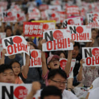 Protesters shout slogans as they hold signs during a rally denouncing Prime Minister Shinzo Abe in downtown Seoul on Aug. 15. | AP