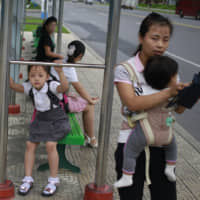 A woman and her children wait for a bus at a stop on Mirae Scientist Street in Pyongyang on Thursday. | AP
