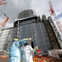 Nuclear workers stand outside the No. 3 reactor building at the Fukushima No. 1 nuclear power plant in Fukushima Prefecture in February. | REUTERS