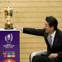 Prime Minister Shinzo Abe points at the Webb Ellis Trophy during a courtesy call by World Rugby officials at Abe\'s official residence in Tokyo on Thursday. | AFP-JIJI