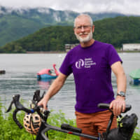 Patrick McIntosh, 63, poses for a photo with his bicycle near Lake Kawaguchi in Yamanashi Prefecture, on Monday. | OSCAR BOYD