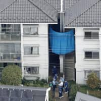 Investigators stand outside an apartment complex in the city of Saitama on Wednesday where the body of a 9-year-old boy was found. | KYODO