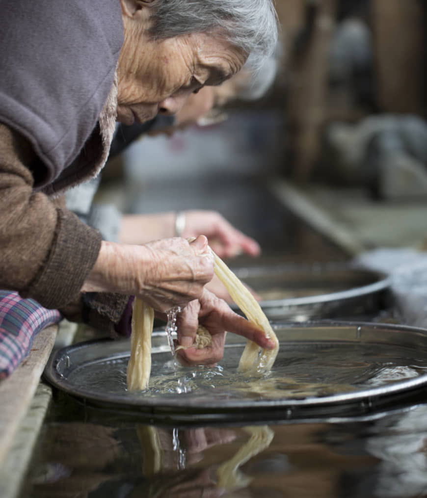 High standards: Clean, cold well water flows through the workshop. Here, Hagi Suzuki and Mariko Furuta perform the task of removing dirt from bark strips. Not even the slightest impurity can remain if Honmino-shi is to meet expectations. | MASASHI KUMA