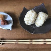 \"I will have this meal\": A pair of chopsticks sit horizontally in front of brown rice onigiri (rice balls) and a homemade pickled plum with miso. | MOMOKO NAKAMURA