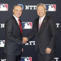 MLB commissioner Rob Manfred (left) and Jun Sawada, president and CEO of Nippon Telegraph and Telephone Corp., shake hands in New York on Wednesday after announcing a technology partnership. NTT will provide its Ultra Reality Viewing technology, which synthesizes video from multiple cameras to create a high-definition, 180-degree image. | KYODO
